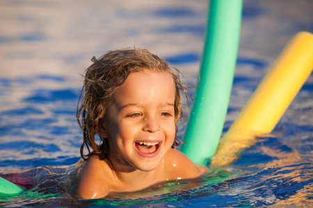 happy child in the pool, learning to swim with swimming noodle; warm sunset lightの写真素材