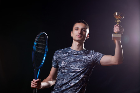 young professional tennis player holding a trophy, blue racket, black backgroundの写真素材