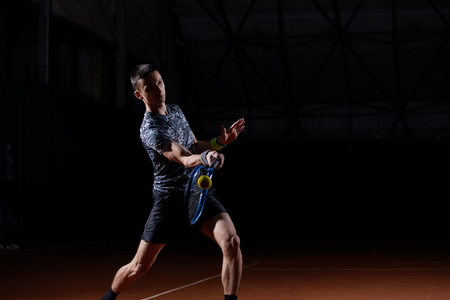 young professional tennis player with a blue racket hitting a forehand, black backgroundの写真素材