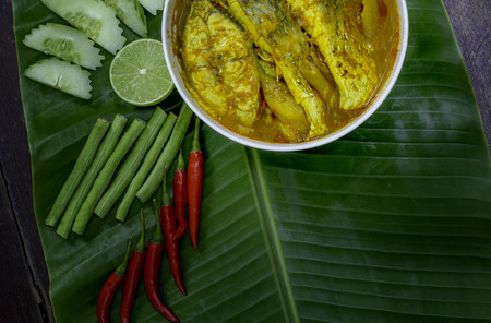 Yellow curry snapper fish with Lotus Stems, Southern Thai Spicy food and fresh vegetable in white dish on banana leaf / selective focusの写真素材