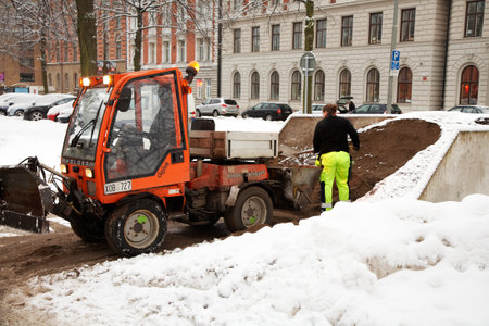 Stockholm Sweden - December 19, 2012: The driver of the mini-tractor with a snowplow on Valhallavägen loading sand for de-icing of walkways.

のeditorial素材