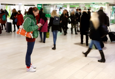 A young woman standing used a smsrt phone at the Centrsl station in Stockholm Sweden.