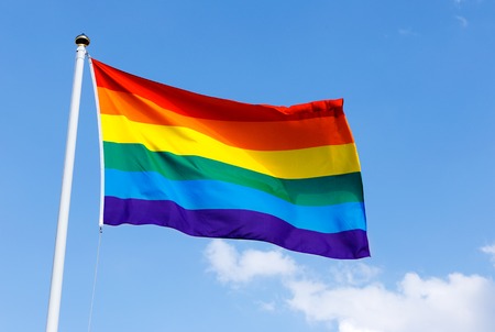 Rainbow flag proudly waving against the blue sunny skiesの写真素材