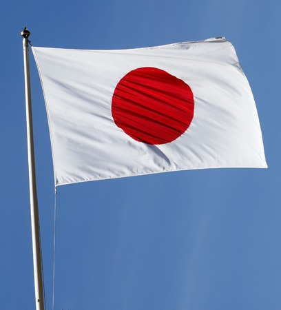 The flag of japan hoisted against blue sky.