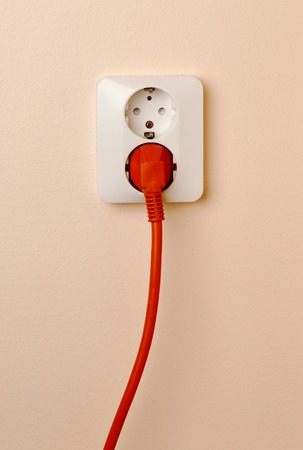 Wall mounted outlet with a red power plug inserted.