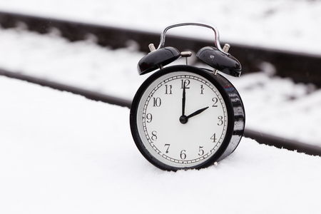One black alarm clock at railroad tracks outdoors in snow.の写真素材