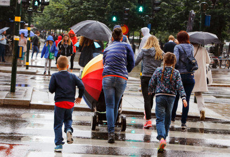 Stockholm, Sweden - July 29, 2015: Rain at a pedestrian crossing on the street Hamngatan, where a woman with a stroller has a rainbow patterned umbrella.のeditorial素材