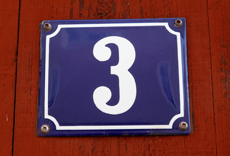 Number three on a blue plate mounted on red wooden wall.の写真素材