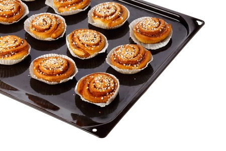 Cinnamon buns in tins of greaseproof paper on a baking tray on white.の写真素材