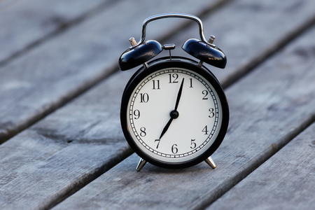 Black alarm clock with white dial on a table showsa few minutes past seven.の写真素材