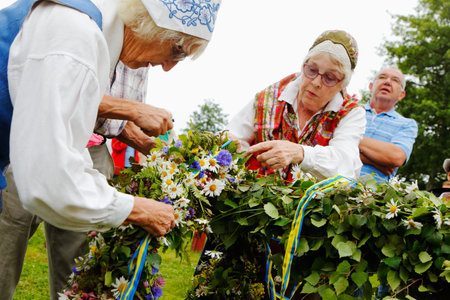 Mariefred, Sweden - June 24, 2016: Two elderly women in traditional costumes attach one of the garlands on the maypole before the rising of the rod at the tradidionellt public midsummer celebration.のeditorial素材