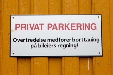 Norwegian sign on a yellow wooden wall informs that it is a private parking and violation results in removal at the owner's expense.の写真素材