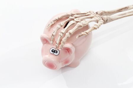 Skeleton holding his hand in a pink piggy bank.の写真素材