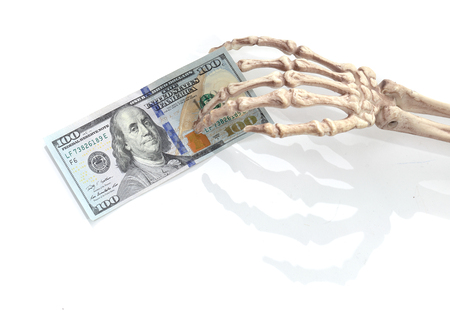 Skeleton hand holding a 100 US dollar bank note on white.の写真素材