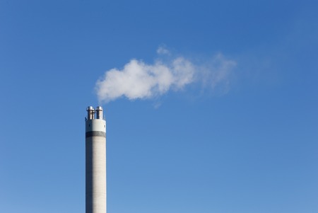 White smoke coming from a chimney constructed of concrete against the blue sky.の写真素材