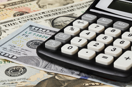 Close-up of a black electronic pocket calculator on U.S banknotes in various denominations.の写真素材