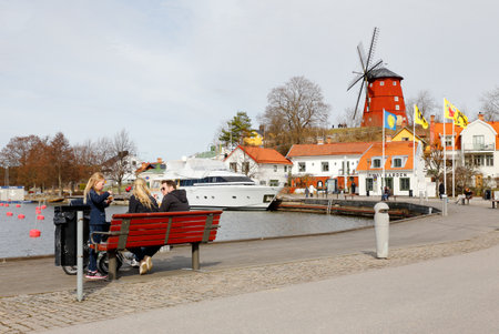 Strangnas, Sweden - April 2, 2017:A family at a park bench on at the empty marina with a windmill on the hill in the background.のeditorial素材