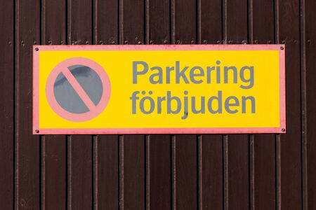 Faded yellow Swedish no parking sign on brown wooden wall.の写真素材