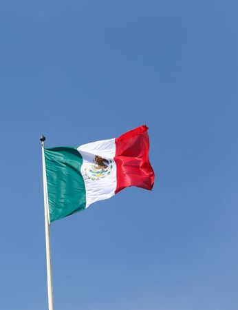The national flag of Mexico hoisted against a blue sky.の写真素材