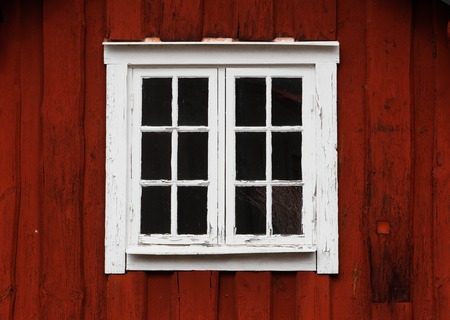 Close up of an older closed window with white window sprint on a red-painted wooden wall.の写真素材