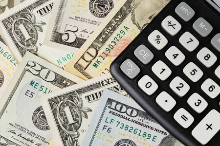 US Dollars banknotes under a black calculator.の写真素材