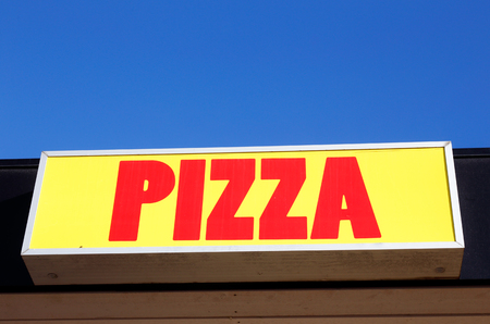 Pizza sign with red text on yellow background with blue sky above.の写真素材
