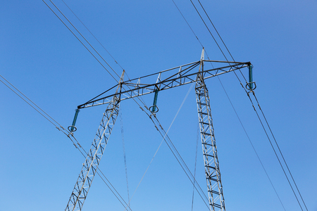High voltage power line with a pylon isolated against a blue sky.の写真素材