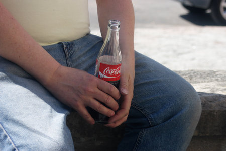Hallstahammar, Sweden - May 30, 2010: Close-up of a relaxed man sittining holding a half empty Cocoa-Cola glass bottle in his hands.のeditorial素材