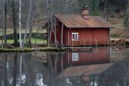 Small red old wooden wash-house near the ice covered lake.の写真素材