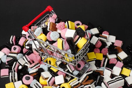 Miniature shopping cart filled and surronded with English liquorice candy.の写真素材