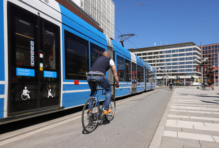 Stockholm, Sweden - May 12, 2021: A man is cycling in central Stockholm next to a modern tram on line 7 at the Sergels torg square.のeditorial素材