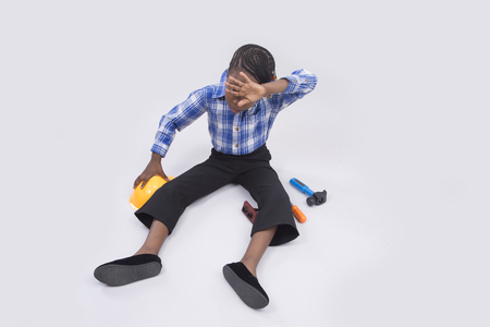 A little girl sitting down and looking tired with hand on her foreheadの写真素材