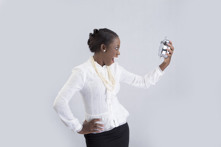 Businesswoman looking at alarm clock with hand akimboの写真素材