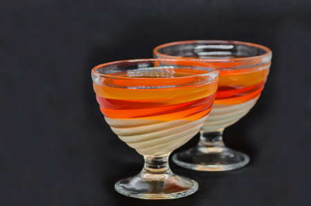 sweet delicious dessert of a multi-colored jelly in a glassware isolated on a black backgroundの写真素材