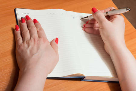 Female hands with manicure over pages of a notebook hold a pen