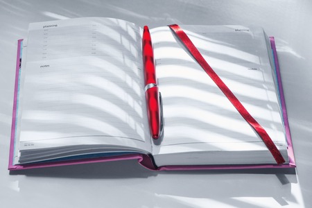 Notebook and ball-point pen on a window sill with light and shade from blindsの写真素材
