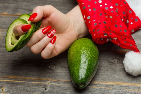 The female hand with beautiful festive New Years manicure holds the avocado fruit cut by ringsの写真素材