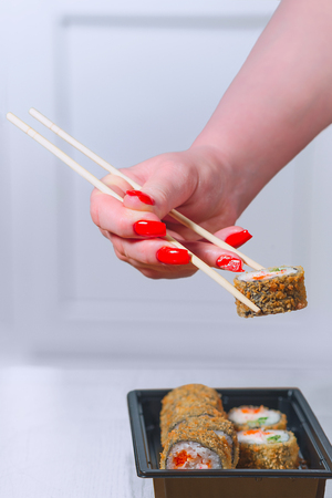 The female hand with magnificent manicure takes sushi from a black plate by means of wooden sticksの写真素材