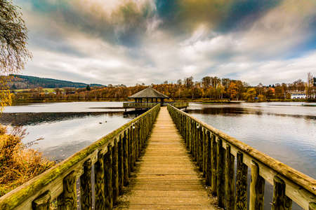 amazing view of a wooden path leading to a gazebo in the middle of the Doyards lake in Vielsalm on a wonderful and cloudy autumn day in the Belgian Ardennesの写真素材