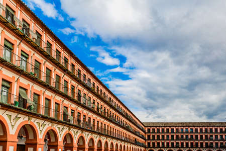 Plaza de la Corredera with its windows, balconies and arches with a combination of brown and orange colors with a blue sky and white clouds in Cordoba Spainの写真素材