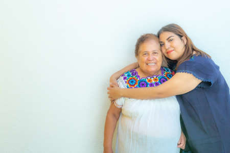 Granddaughter hugging her grandmother, two smiling Mexican women on a white background, space for...