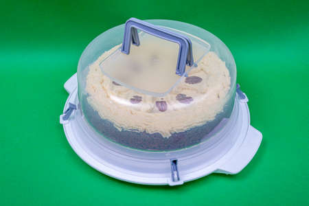 Round transparent plastic cake cover box with gray handles on the top for transportation with a cake...