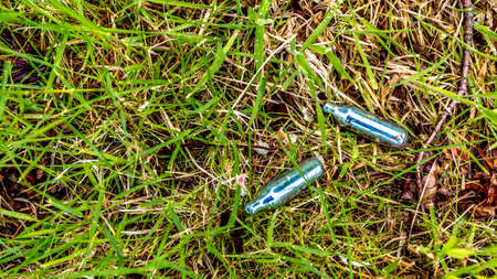 Empty bulbs of nitrous oxide or laughing gas on the grass in a public park, hippie crack is used as a recreational drug or as a party drugの写真素材