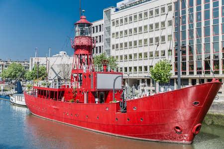 Red boat anchored at the quay of the port of Wijnhaven in the center of Rotterdam with buildings in the background, sunny day with a blue sky in the Netherlands Hollandのeditorial素材