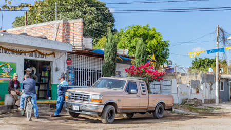 Guadalajara, Jalisco, Mexico. January 14, 2020. Group of men chatting outside an auto parts store, one grocery stores next to old and deteriorated houses, truck parked on an unpaved streetのeditorial素材