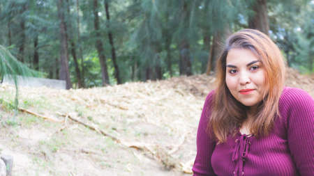 Young Mexican woman with a tender expression looking at the camera with modern natural makeup, trendy eyebrows, long hair, purple blouse in the park with trees in the backgroundの写真素材