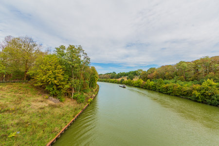 Juliana canal surrounded by lush trees with yellow green foliage, freighter sailing on calm waters, sunny day with many white clouds between Elsloo and Mers in South Limburg, Netherlands Hollandの写真素材