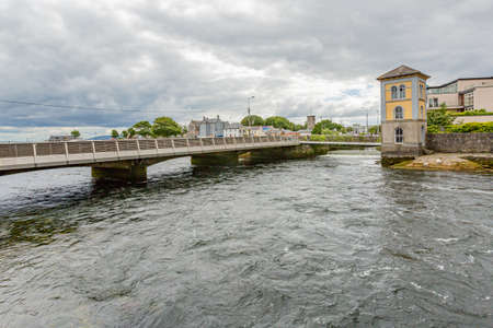 Wolfe Tone Bridge over the River Corrib with its flowing waters and the Galway Fisheries Watchtower Museum in the background, Galway Waterways, cloudy day in Galway City, Connacht Province, Irelandのeditorial素材
