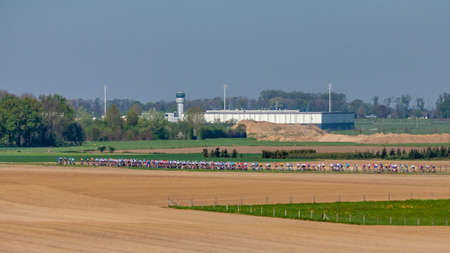 Group of cyclists pedaling on a road in a cycling competition between farm fields and an airport in the background, wonderful spring day in the countryside in south Limburg in the Netherlandsの写真素材