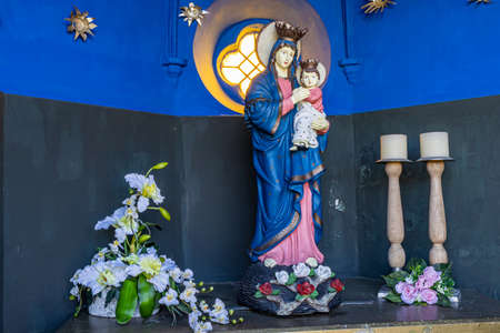 Beek, South Limburg, Netherlands. November 18, 2020. Lady Chapel Kelmond with the Statue of the Virgin Mary with the child Jesus, flowers and two candles, blue walls and a window in the backgroundのeditorial素材